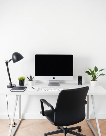 workplace with computer, lamp and plant in vase at white wall