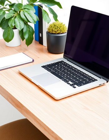 Laptop on a wooden desk with a notebook and a flower in a pot