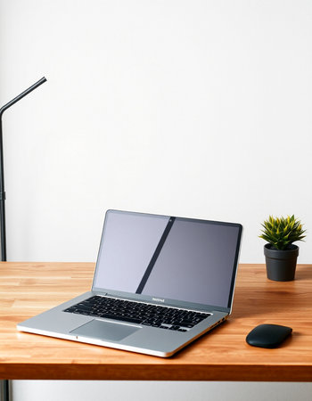 Laptop on wooden table with lamp and plant on white wall background