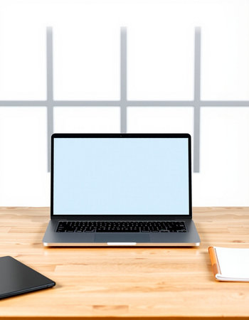 Laptop with blank blue screen on wooden table in front of window