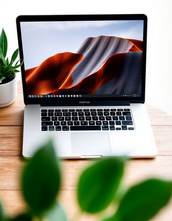 Laptop on wooden desk with red sand dunes and green plants