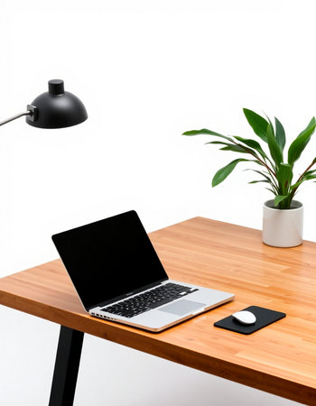 Laptop on a wooden table with a lamp and a plant on a white background