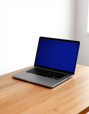 Laptop with blank screen on a wooden table in front of white wall