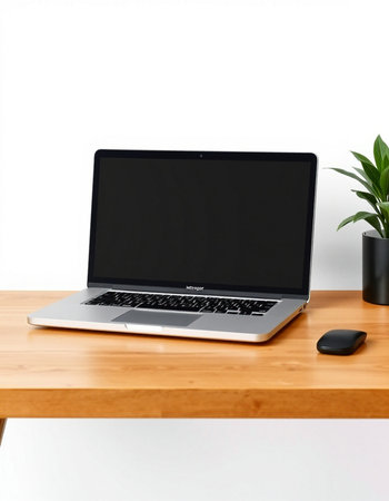 Laptop on a wooden table with a white wall and a plant
