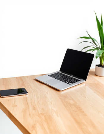 Laptop with blank screen on wooden table and smartphone on white wall background