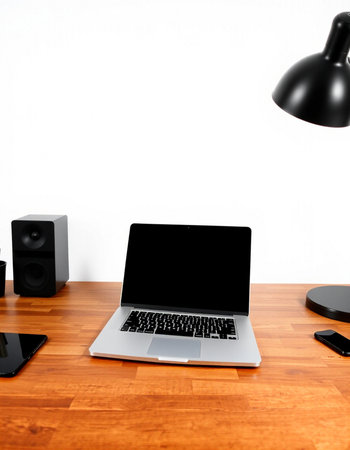 Laptop with blank screen on wooden desk and black speakers on white wall background