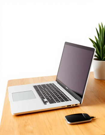 Laptop on wooden desk with smartphone and plant on white background.