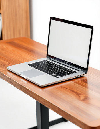Laptop with blank screen on wooden table and white wall background.