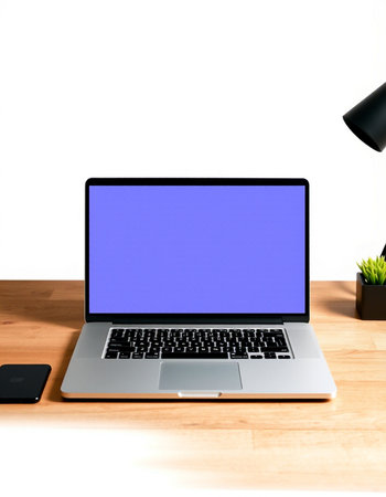 Laptop with blank screen on wooden desk with lamp and mobile phone