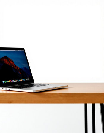 Laptop on a wooden table with white wall in the background.