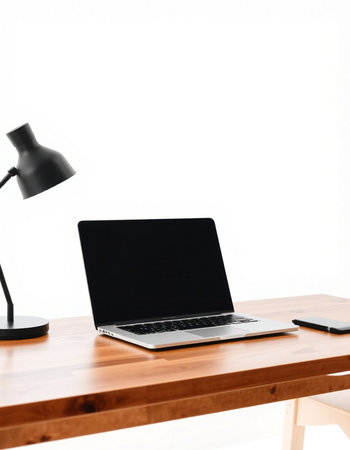 Laptop computer with blank screen on wooden table and black lamp on white wall backgroundの写真素材