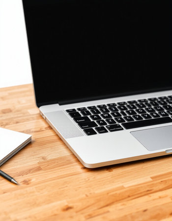 Laptop on a wooden desk with a notebook and a pen.
