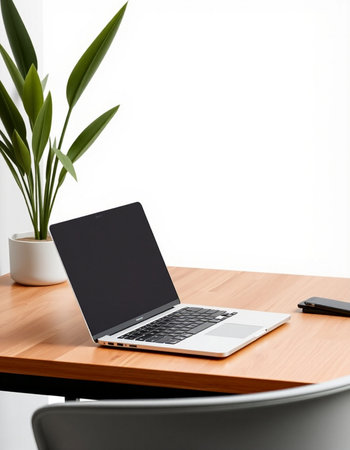 Laptop with blank screen on a wooden table with a plant in the background