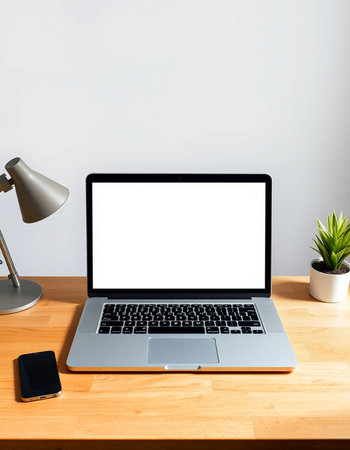 Laptop with blank white screen on wooden table with lamp and plant