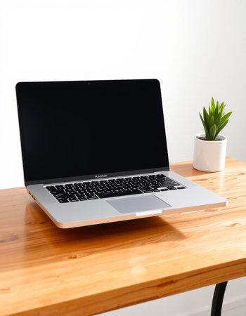 Laptop with blank screen on wood table and white wall background.