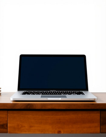 Laptop with blank screen on a wooden table against a white wall
