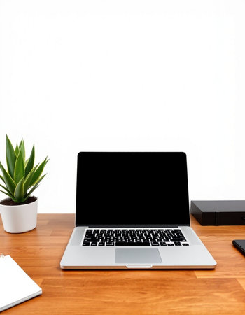 Laptop with blank screen on wooden table and white wall background.