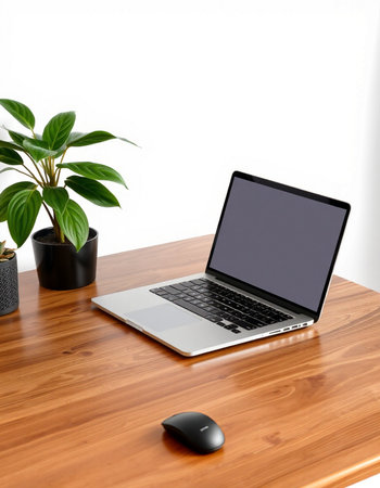 Laptop with blank screen on a wooden table and a green plant