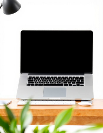 Laptop with blank screen on wooden table and white wall background.