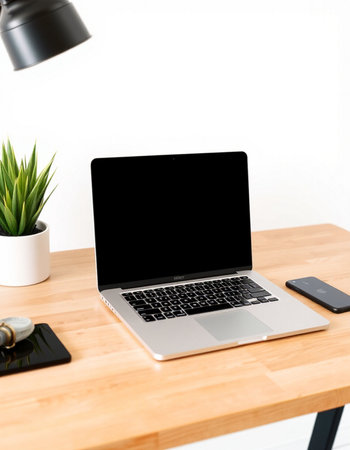 Laptop with blank screen on wooden table and white wall background.