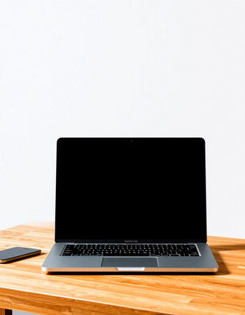 Laptop with blank screen on wooden table and white wall background.
