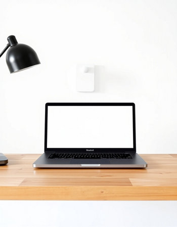 Laptop with blank screen on wooden table and white wall background.