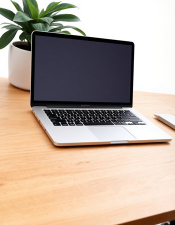 Laptop with blank screen on a wooden table with a plant in the background