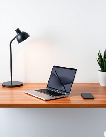 Laptop with blank screen on wooden table and black lamp on white wall backgroundの写真素材