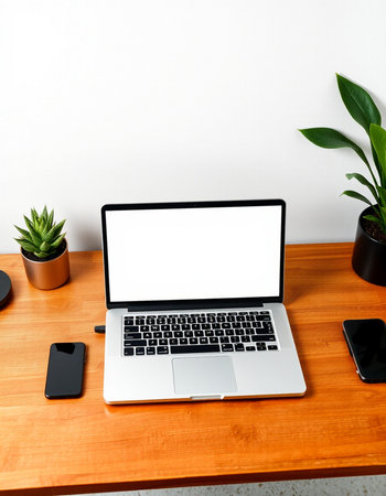 Mockup image of laptop with blank white screen on wooden desk with smartphone and plantの写真素材