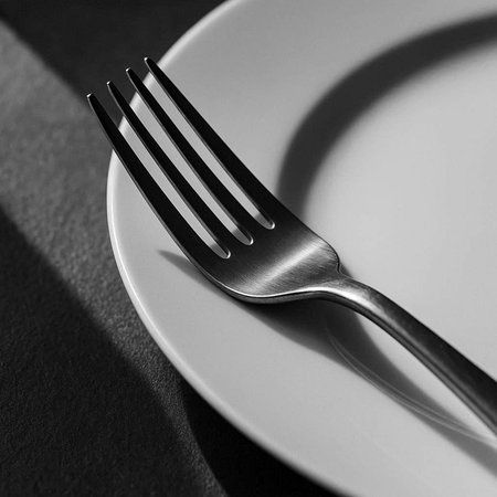 Fork on a white plate with shadow on a black background.の写真素材
