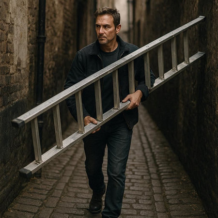 Portrait of a man in a black T-shirt and jeans with a metal fence on the street.の写真素材