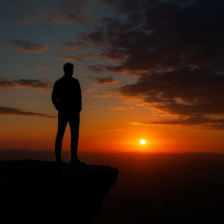 Silhouette of a man standing on top of a mountain at sunset