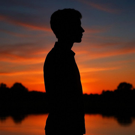 Silhouette of a young man standing in front of a sunset