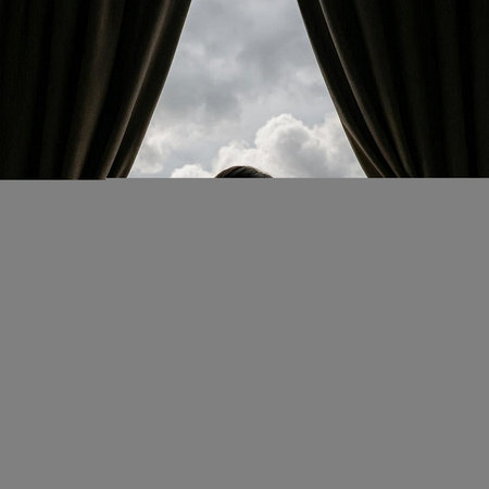 A man looking out the window with a cloudy sky in the background.の写真素材