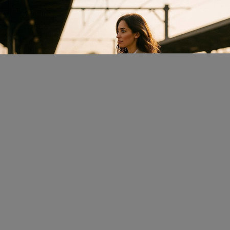 Beautiful young brunette woman in a black dress walking on the train station.
