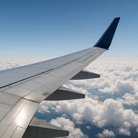 Wing of an airplane flying above the clouds. Blue sky background.