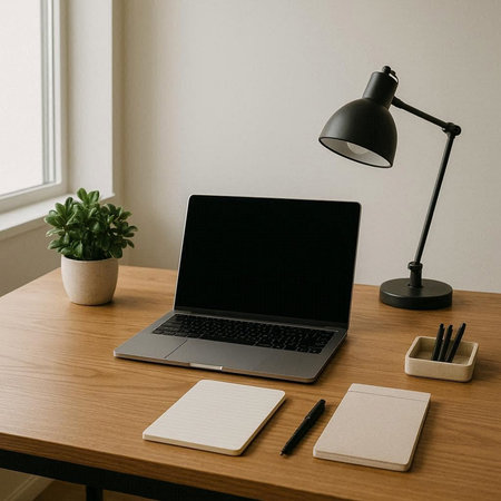 Laptop with blank screen and stationery on wooden table in office