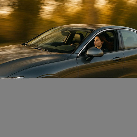 Young woman driving a car on the road at sunset in autumn.