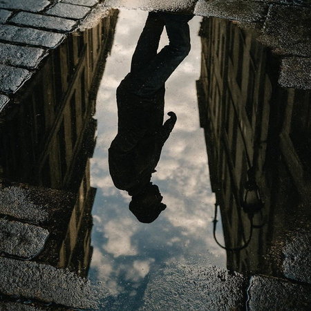 Reflection of a man in a puddle on the street.
