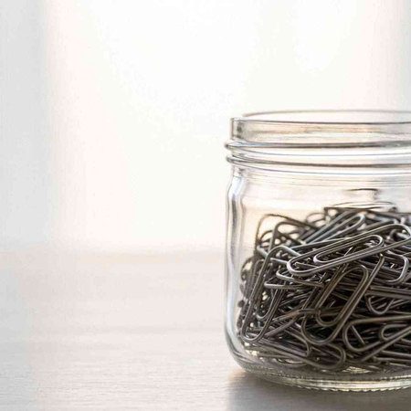 Paper clips in a glass jar on a white background. Copy space.