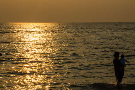Woman with a baby on hands at sunset on  the beach bangsaen Thailandの写真素材