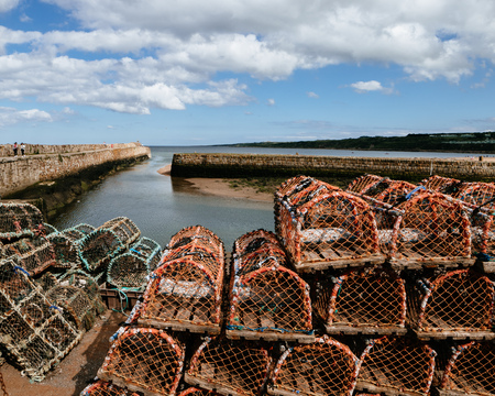 tall stacks of lobster traps on a harbour in Scotland with a long pier streching out to seaのeditorial素材