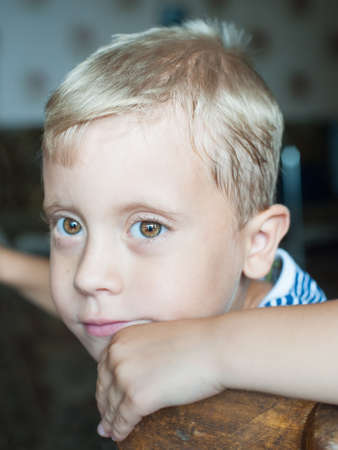 Beautiful cute young boy thinking sitting on chairの写真素材