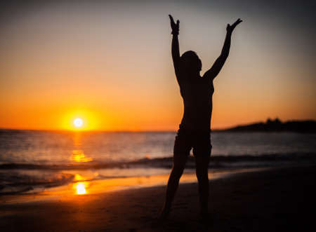 Happy boy at sunset with hands raisedの写真素材