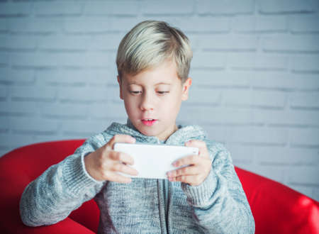 Cute blond boy playing with a smartphoneの写真素材