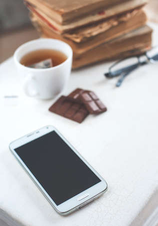 Tea, chocolate, old books and smartphoneの写真素材