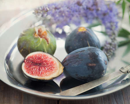Whole and sliced figs on a plate and on a wooden table. Beautiful still lifeの写真素材