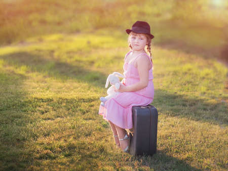 little girl in a hat sits on a suitcaseの写真素材
