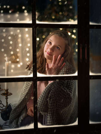 Cute girl outside the window at his home in anticipation of New Year miracle.の写真素材