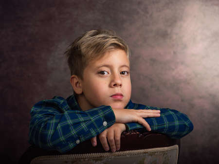 Beautiful little boy, blonde, sad, leaning on a chairの写真素材